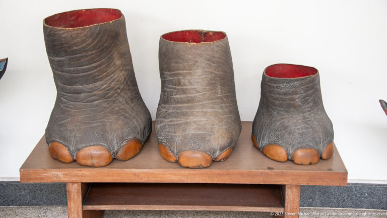 Three dark cylindrical objects shaped like elephant feet, arranged by size on a wooden bench.