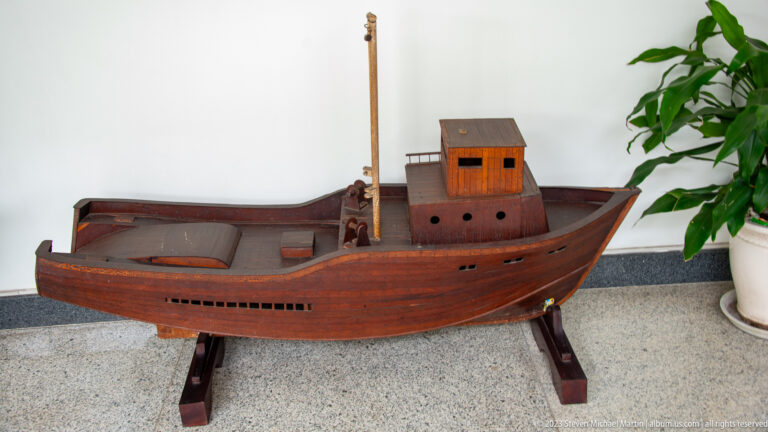 Wooden model of a compact cabin boat with a raised wheelhouse and open deck.