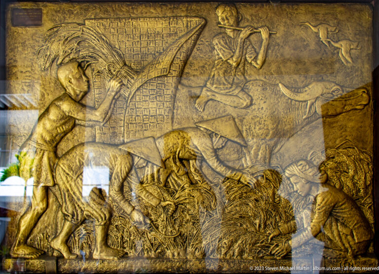 Large gold-toned relief showing armed figures, animals, inscriptions, and a dynamic battle scene.