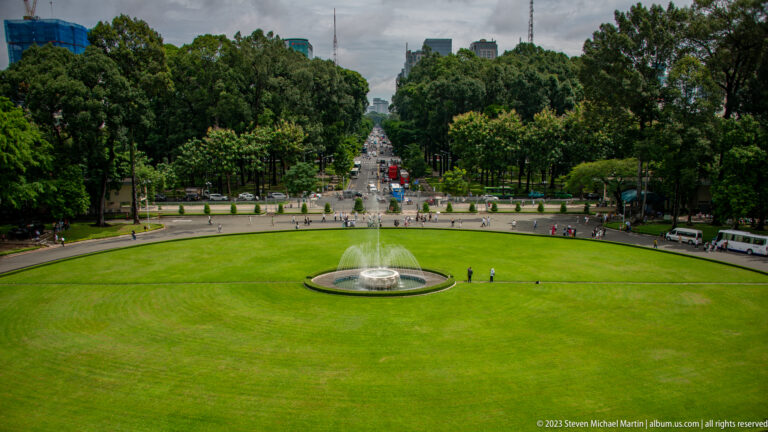 Elevated view over the palace lawn and circular fountain toward a tree-lined city boulevard.