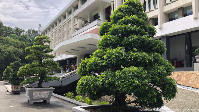 Two cloud-pruned trees in planters beside a sloping ramp and white palace façade.
