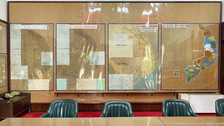 Large military planning maps with overlays behind green chairs and a conference table.
