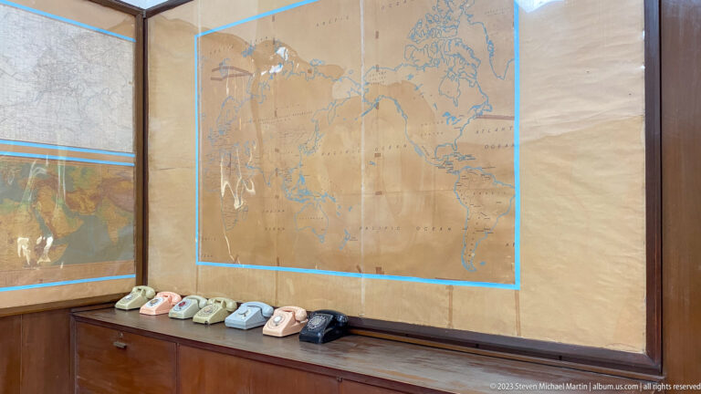 World map mounted above a row of cream, pink, gray, and black rotary telephones.