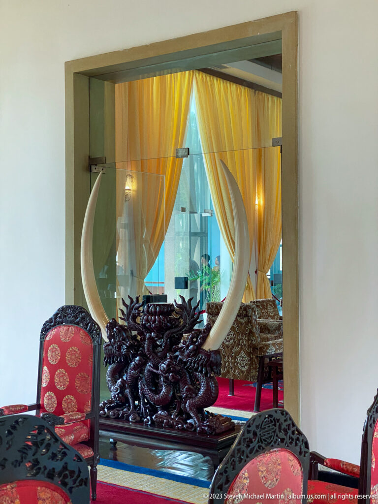 Paired curved tusks on a dark carved dragon stand, framed through a doorway among red chairs.