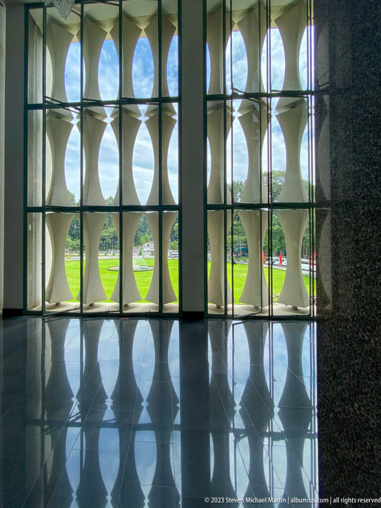 Interior view of repeating oval and hourglass concrete screens reflected on a polished dark floor.