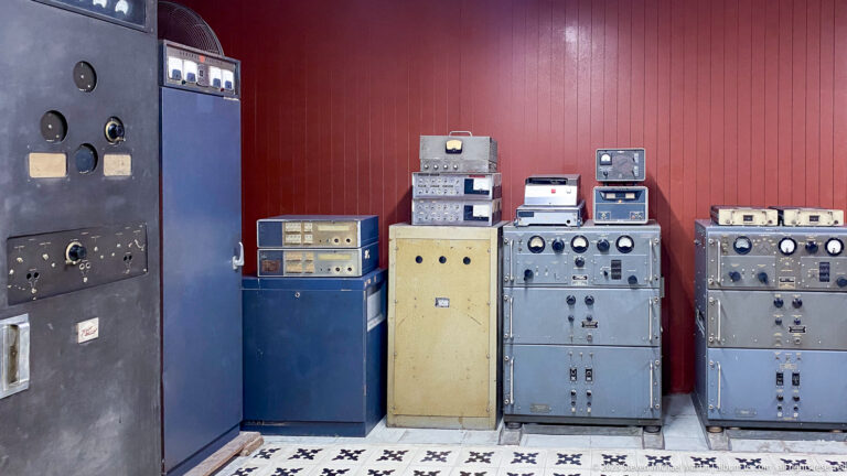 Bank of gray, blue, and yellow radio and control cabinets with meters and switches in the bunker.