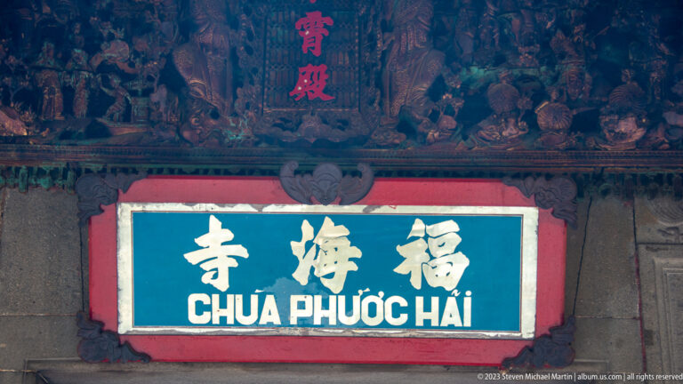 Blue Chùa Phước Hải plaque with Chinese characters beneath a dark carved wooden frieze.