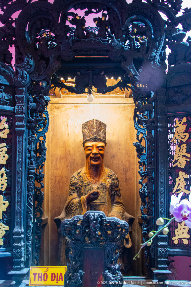 Illuminated bearded Earth God figure seated in a dark carved shrine labeled Thổ Địa.