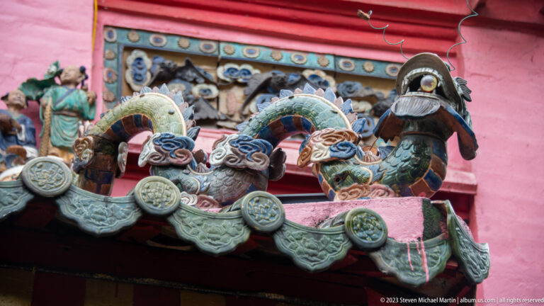 Glazed ceramic birds and coiled creatures projecting from a gray tiled temple roof edge.