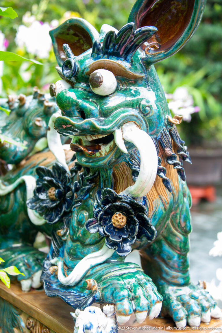 Close-up of a multicolored glazed guardian creature with large ears, curling white tusks, and floral details.