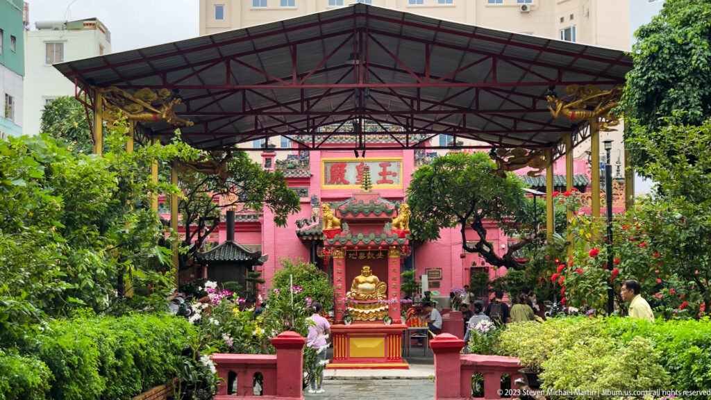 Wide covered courtyard with a central red shrine, garden path, visitors, and dense green planting.
