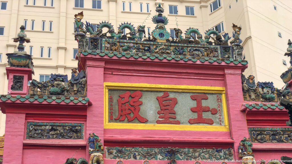 Pink temple gate with a large Chinese inscription and elaborate ceramic dragons and figures along the roofline.