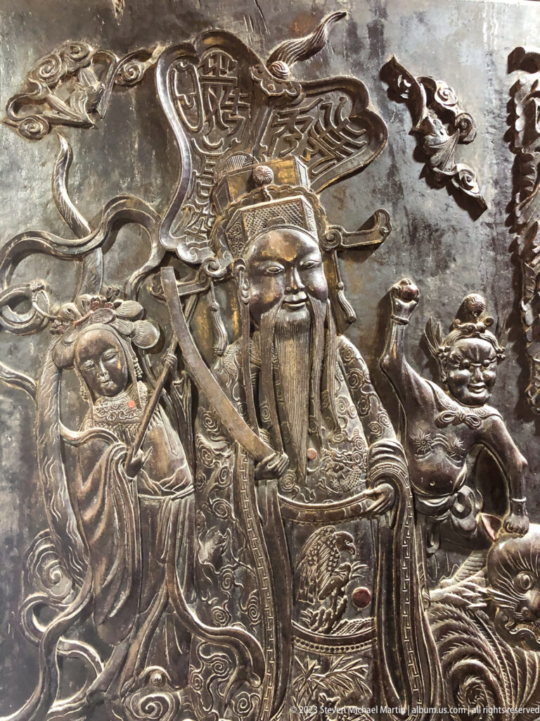Silver embossed relief of a bearded armored figure with attendants, clouds, and mythic animals.