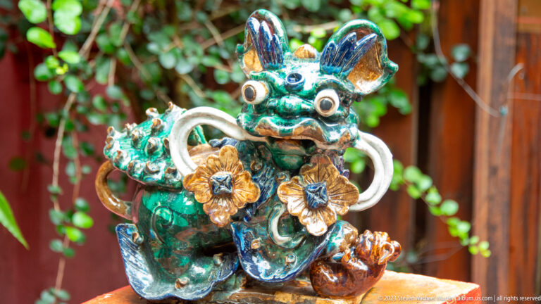 Turquoise and amber glazed guardian creature with large eyes, upright ears, and floral ornament.