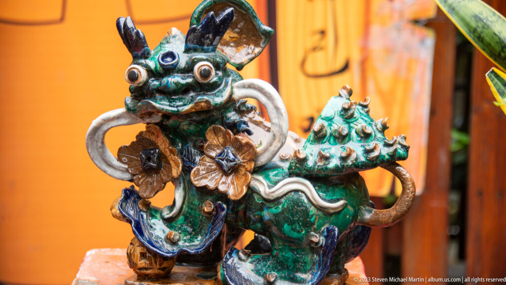 Two multicolored glazed guardian creatures with large eyes and floral decoration against an orange wall.