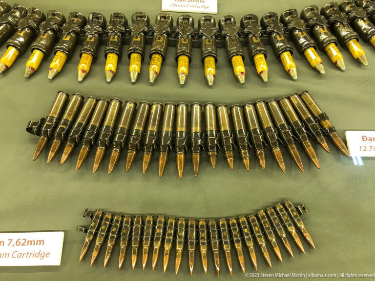 Rows of linked and loose ammunition cartridges in a museum display case.