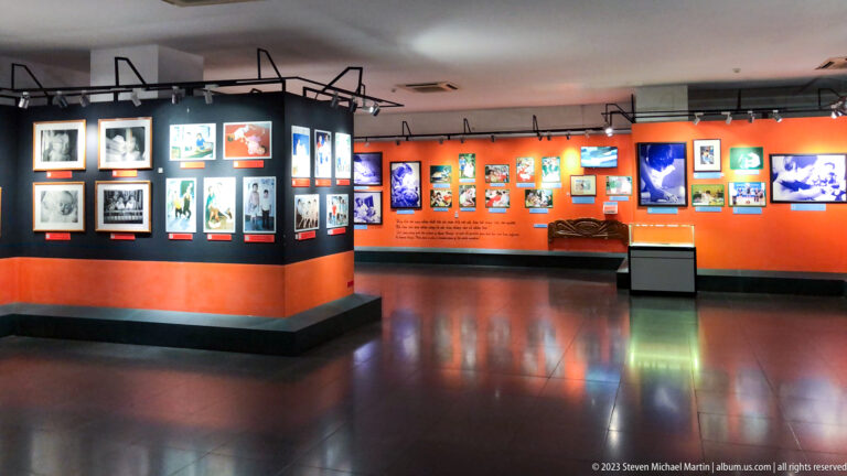 Orange-and-black museum gallery with framed photographs and video screens.