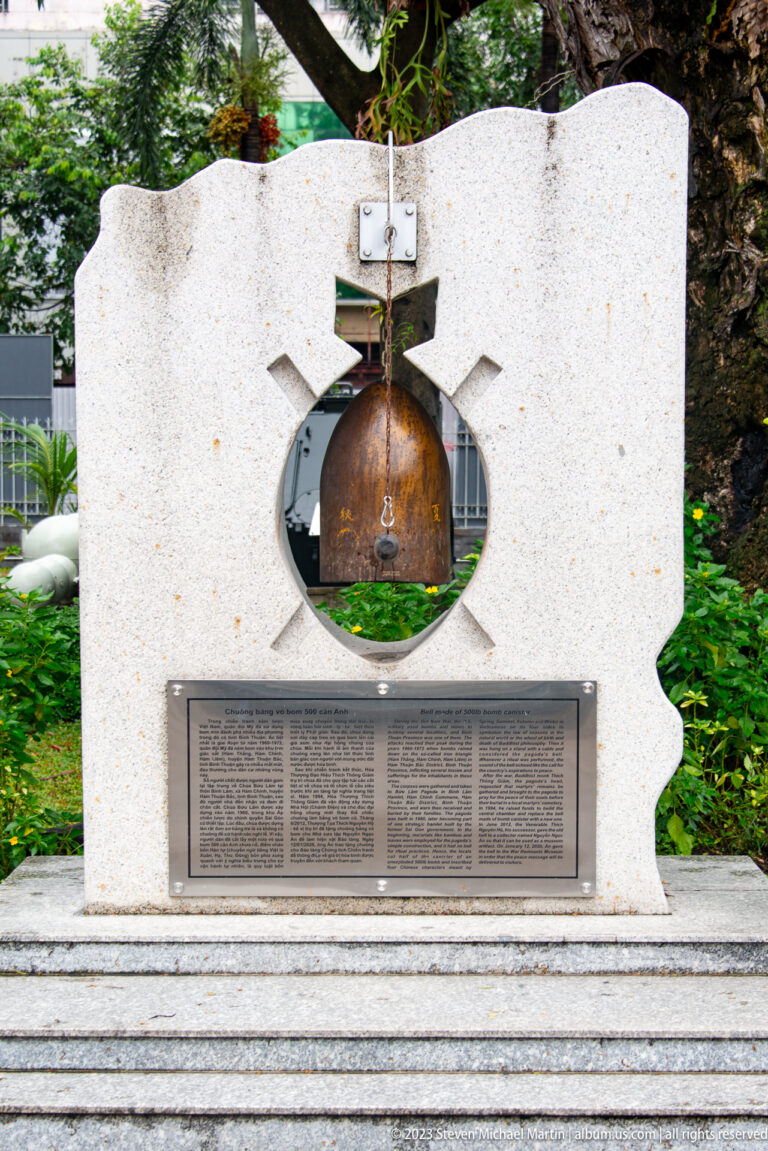 Stone memorial with circular opening, suspended metal element, and inscribed plaque.