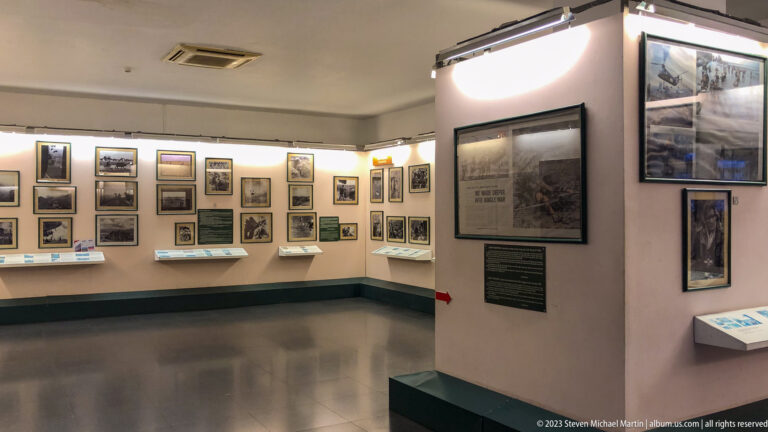 White museum gallery lined with framed historical photographs and text panels.