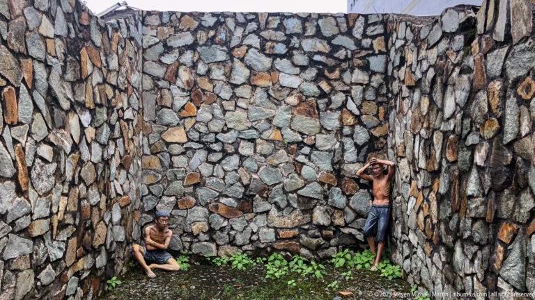 Two prisoner mannequins inside a narrow stone-walled enclosure.
