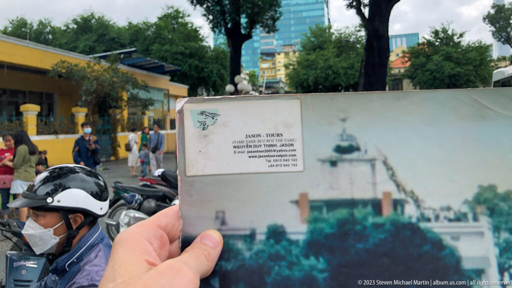 Hand holding a historical building photograph against a modern street scene.
