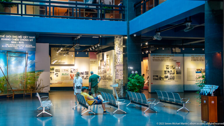 Visitors inside a blue museum hall with historical panels and balcony above.