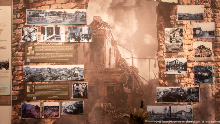 Sepia exhibition panel with archival photographs of bomb damage and destroyed buildings.