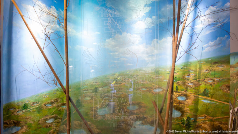 Immersive museum landscape with bare tree trunks and painted countryside.