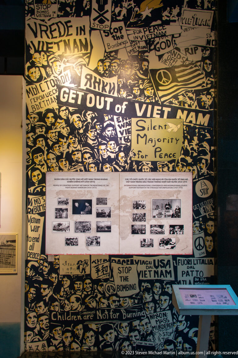 Black-and-yellow antiwar mural with protest slogans and an interpretive display.