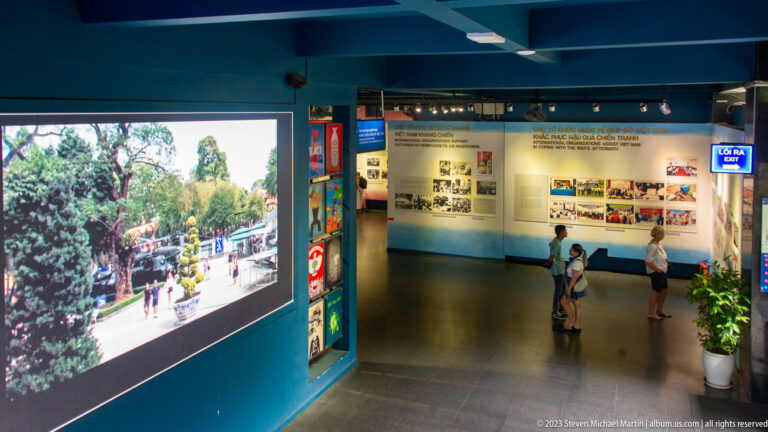 Visitors in a museum gallery beside a large video screen and wall panels.