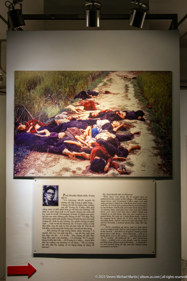 Large color photograph of bodies on a road above a museum text panel.