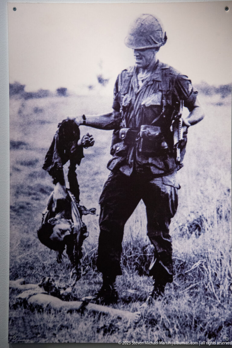 Black-and-white photograph of an armed soldier beside a crouching civilian.