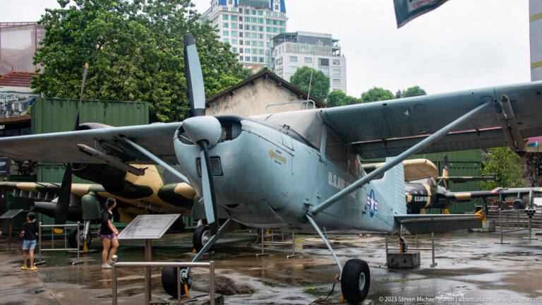 Gray high-wing Cessna O-1 Bird Dog with U.S. markings in the museum courtyard.