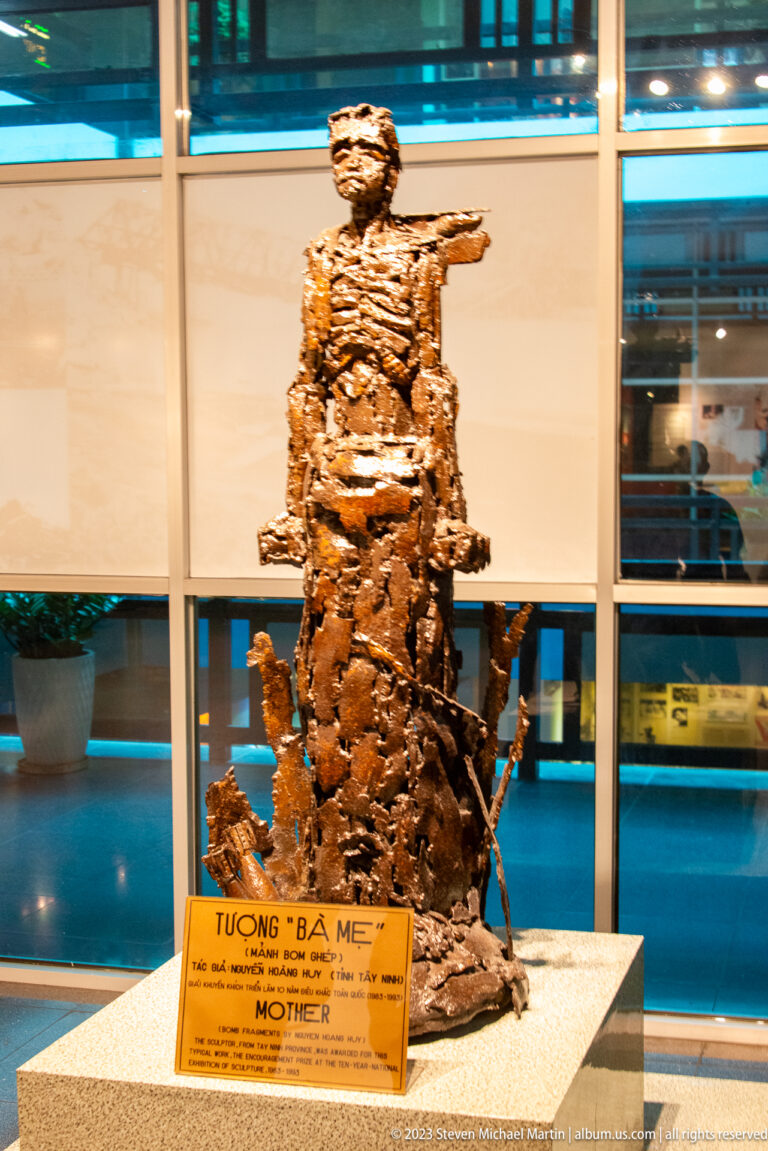 Bronze seated female figure titled Mother on a museum pedestal.