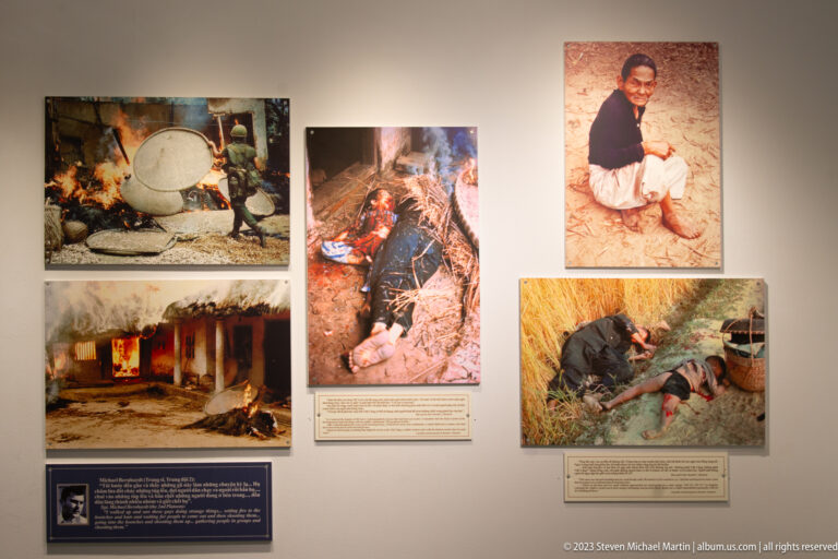 Color photographs of wounded civilians and damaged homes on a museum wall.