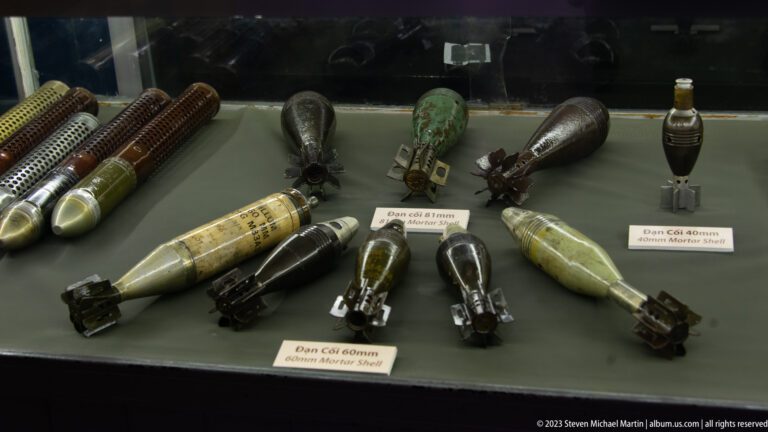 Mortar rounds, grenades, and explosive devices arranged in a museum case.