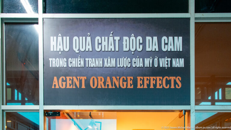 Bilingual black sign reading “Agent Orange Effects” above a gallery entrance.