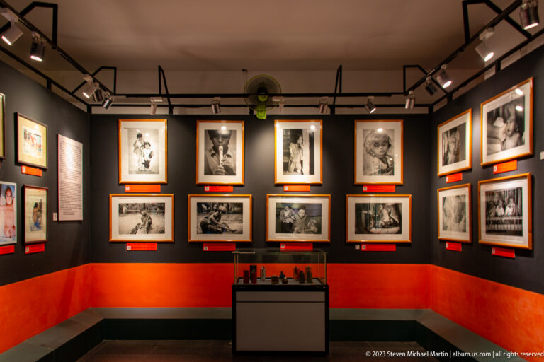 Dark gallery wall with framed portraits and family photographs about Agent Orange.