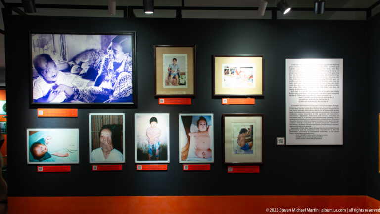 Video screen and framed portraits of children and adults in the Agent Orange gallery.