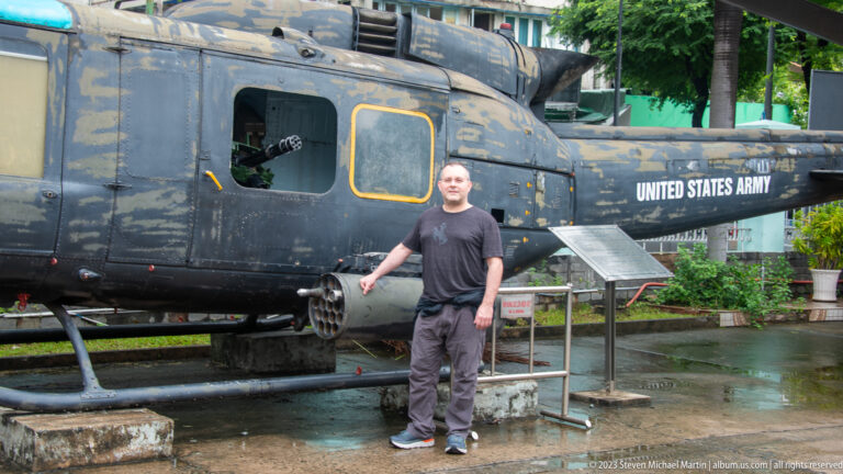 Visitor standing in front of a weathered U.S. Army Huey helicopter.