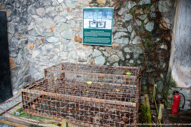 Low rusted wire detention cage beneath an interpretive panel.