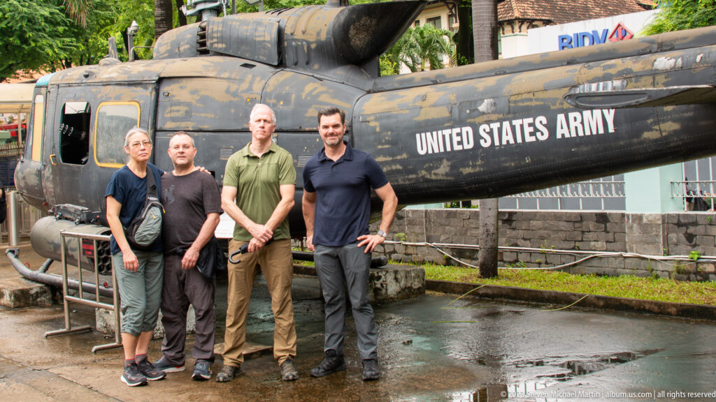 Four visitors standing beside a weathered U.S. Army Huey helicopter.