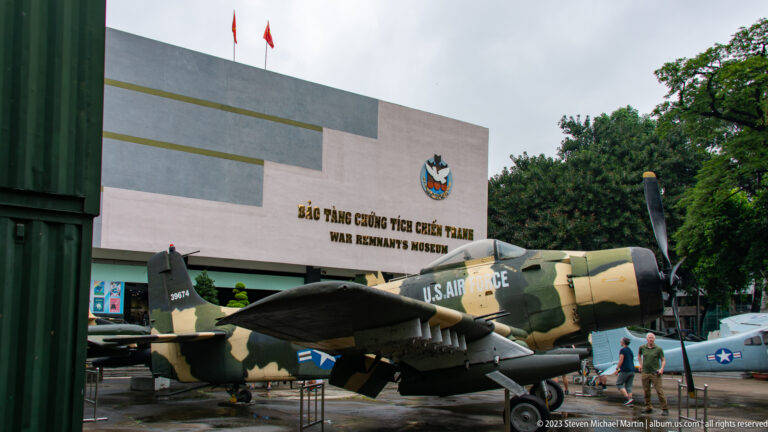Camouflaged A-1 Skyraider in front of the War Remnants Museum façade.