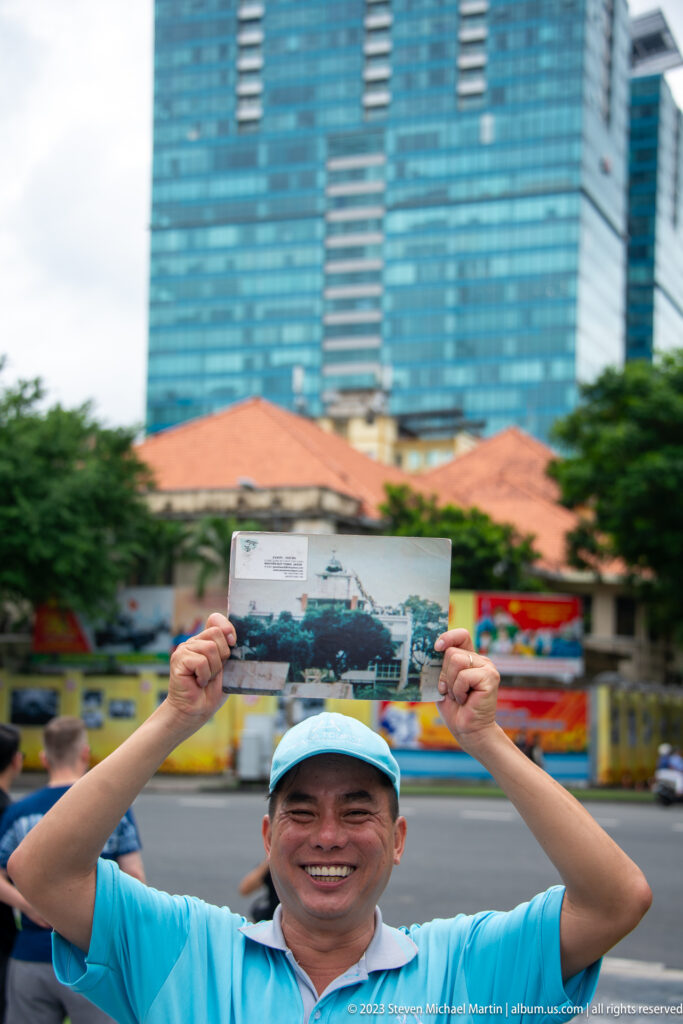 Smiling visitor holding a postcard above his head outside the museum.