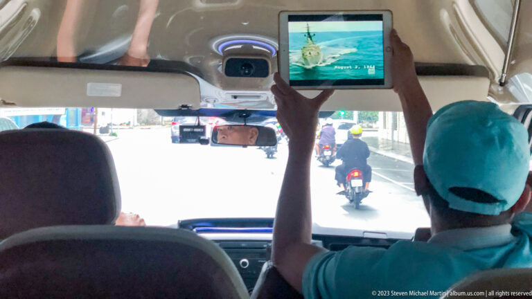 Passenger holding a tablet toward the windshield inside a moving vehicle.