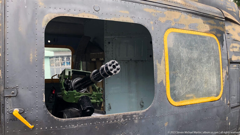 Multi-barrel rotary gun mounted inside the open side of a weathered helicopter.