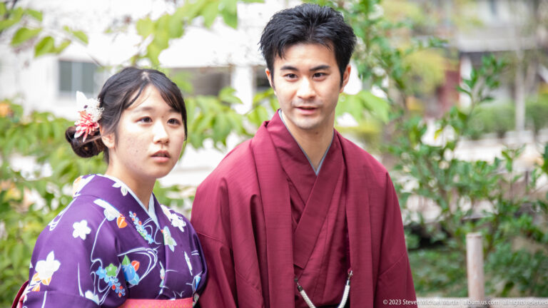 Woman in a purple floral kimono and man in a burgundy kimono standing outdoors near Kanazawa Castle.