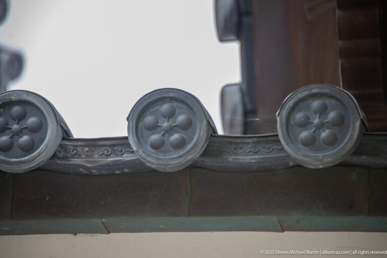 Three round decorative roof-tile ends with raised floral crests beneath a dark Japanese eave.