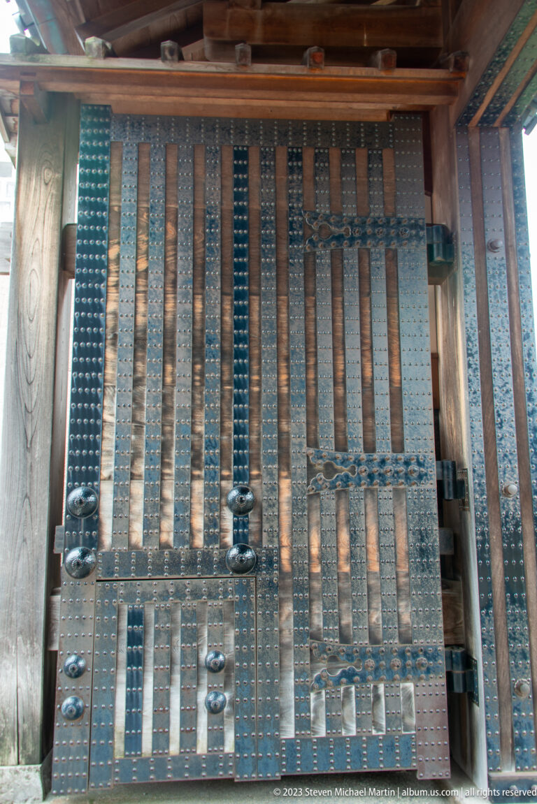 Large wooden castle door reinforced with vertical iron straps, studs, hinges, and rounded fittings.