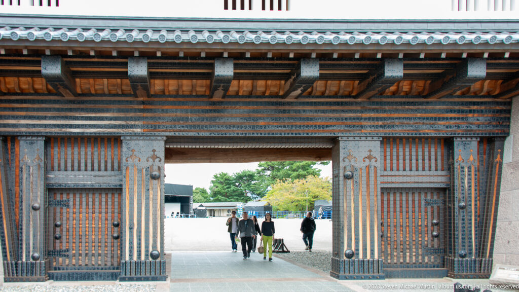 Open studded timber gate framing visitors walking into a bright castle courtyard.